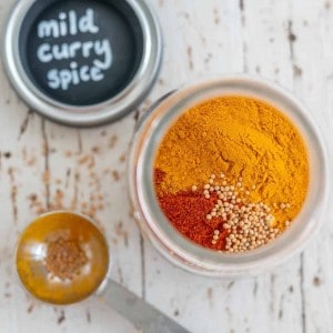 Open jar of spices not mixed together with lid on bench top labeled "mild curry spice"