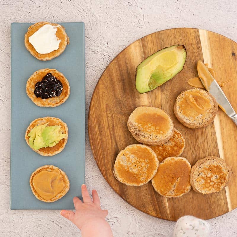 baby hand reaching out for pikelets with various topping