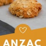 Golden Anzac biscuits on a baking paper lined cookie sheet, with text iverlay.