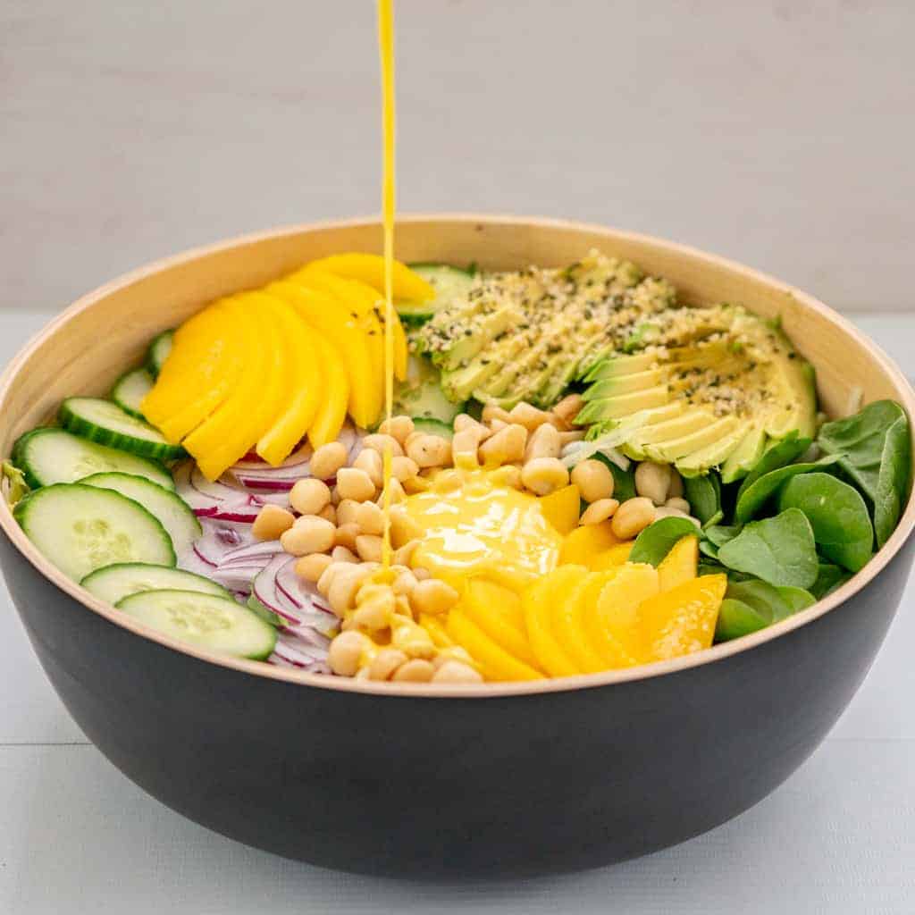 Mango salad dressing being drizzled onto a colourful salad