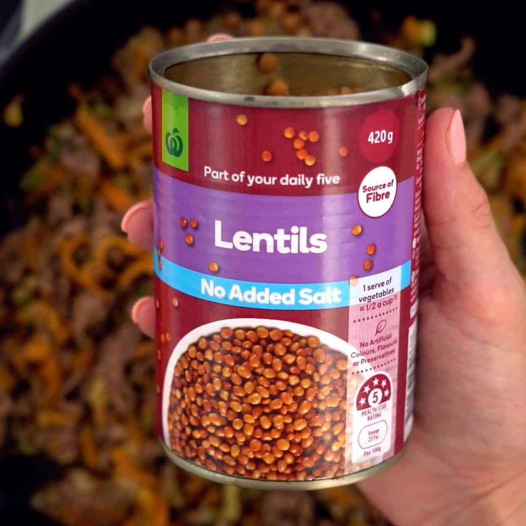 hand holding a can of lentils above a pan of minced beef