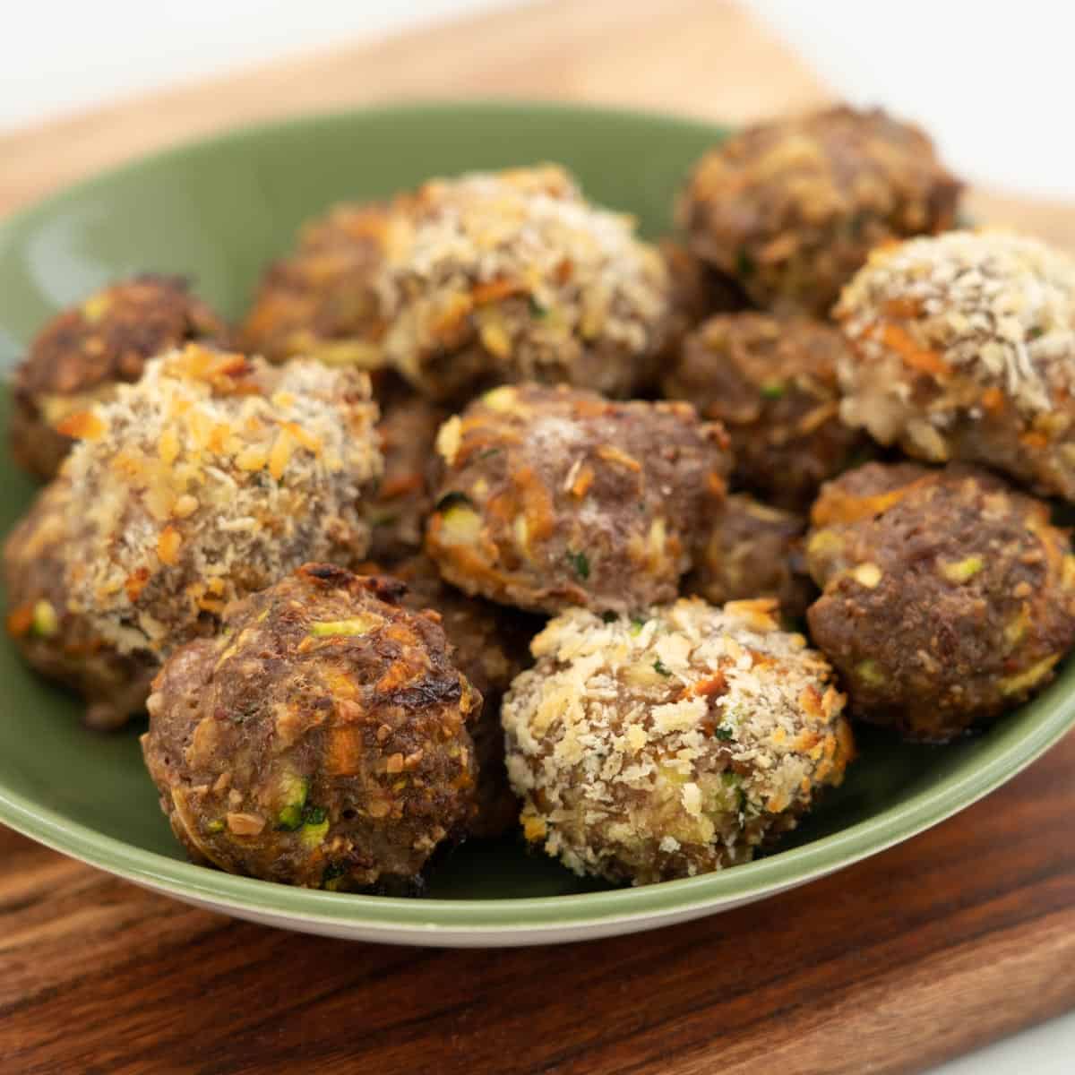 A green ceramic bowl filled with crumbed and non-crumbed rissoles. 