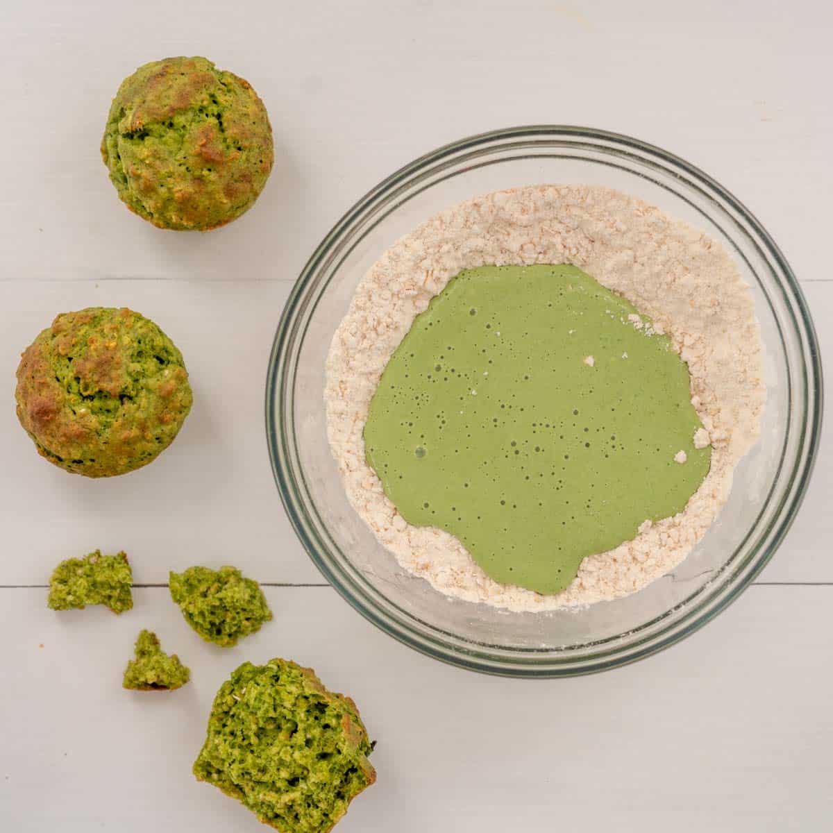 Green smoothie added to the dry ingredients to form the muffin batter, 3 spinach muffins sitting next to the batter bowl