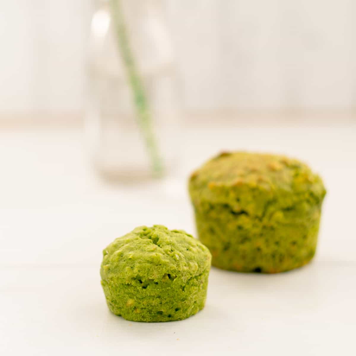 a mini spinach muffin sitting next to a regular sized muffin