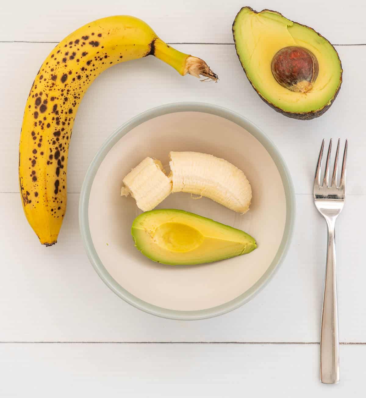 banana and avocado in a bowl with a fork ready to be mashed