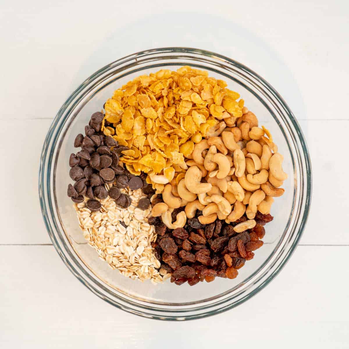 5 cups of ingredients in a bowl: Cornflakes, Cashews, Oats, Raisins, Choc Chips