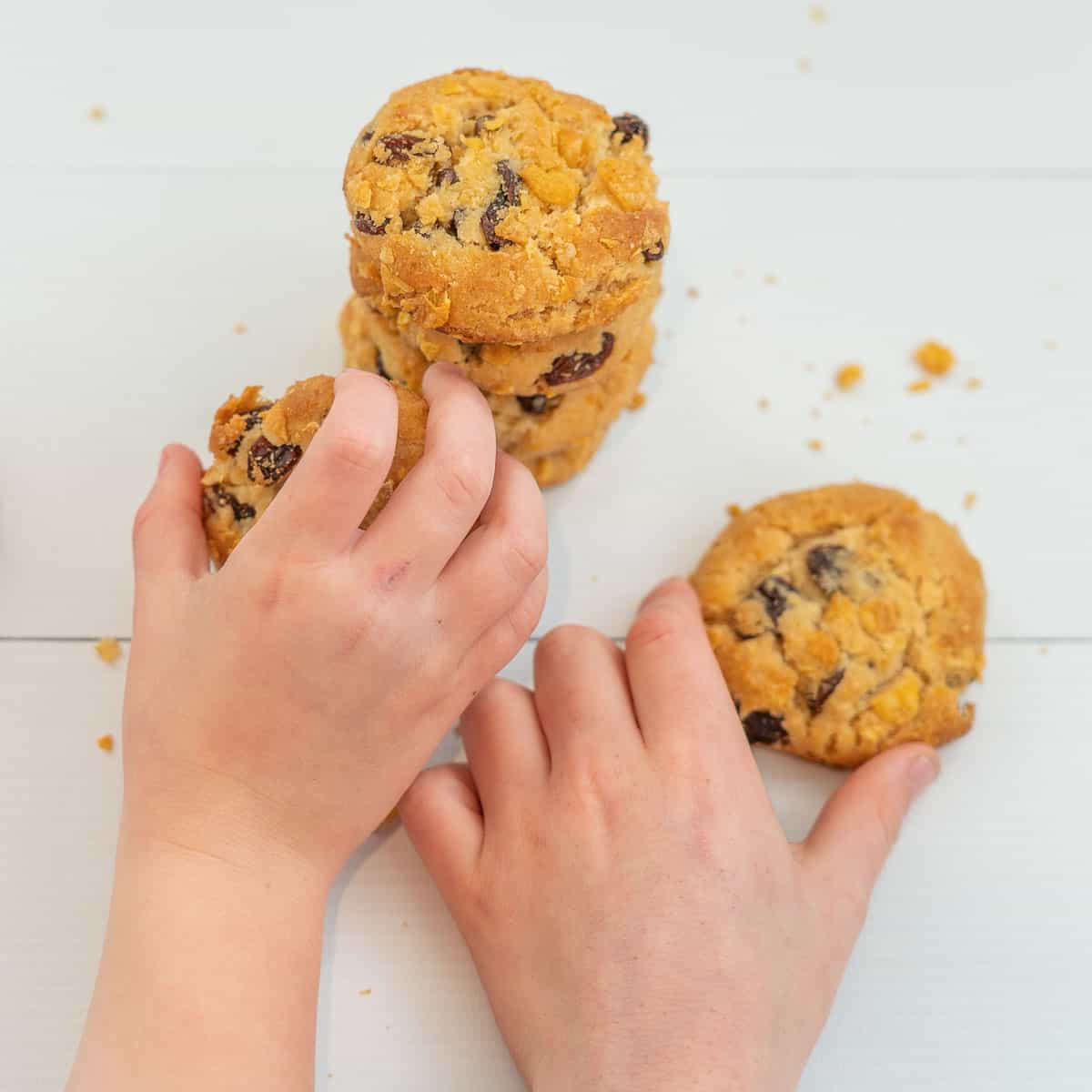 2 children's hands reaching for cornflake and raisin cookies