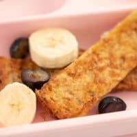 a pink baby breakfast plate with eggy bread, blueberries and sliced bananas