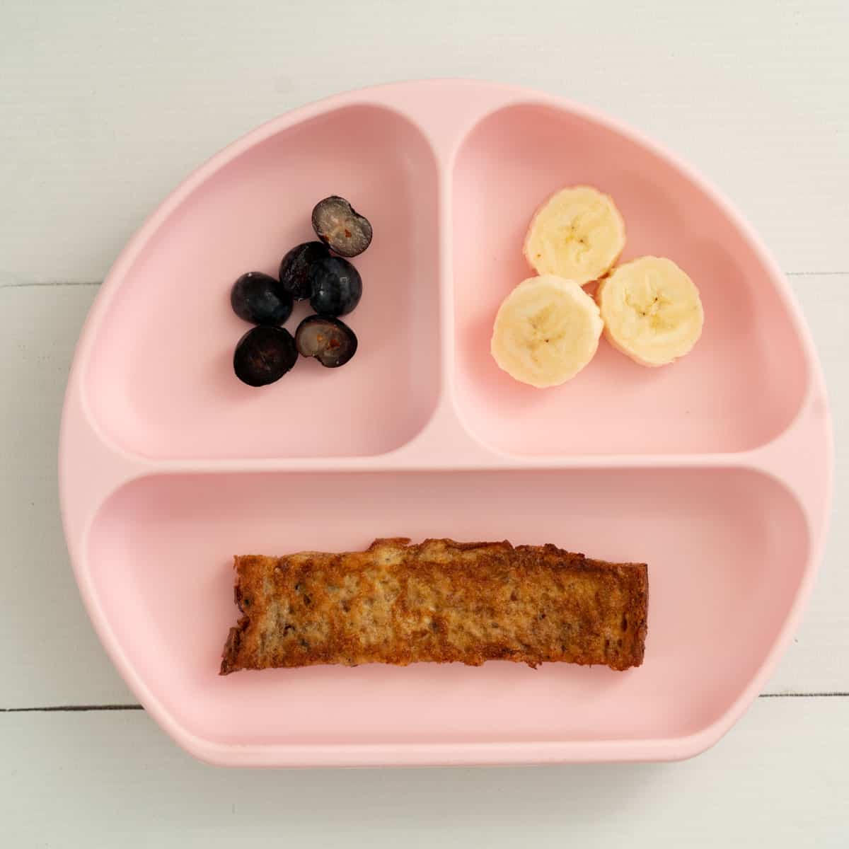 a pink baby breakfast plate with eggy bread, blueberries and sliced bananas