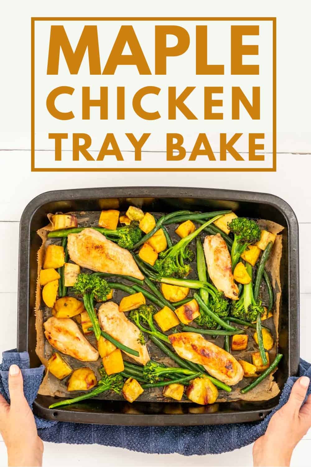 Large black roasting pan of maple chicken tray bake being held by a woman's hands 