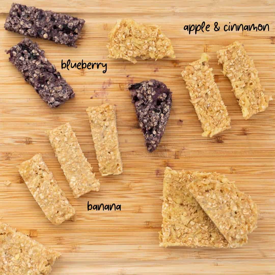 a selection of porridge fingers on a wooden board, apple and cinnamon, banana and blueberry