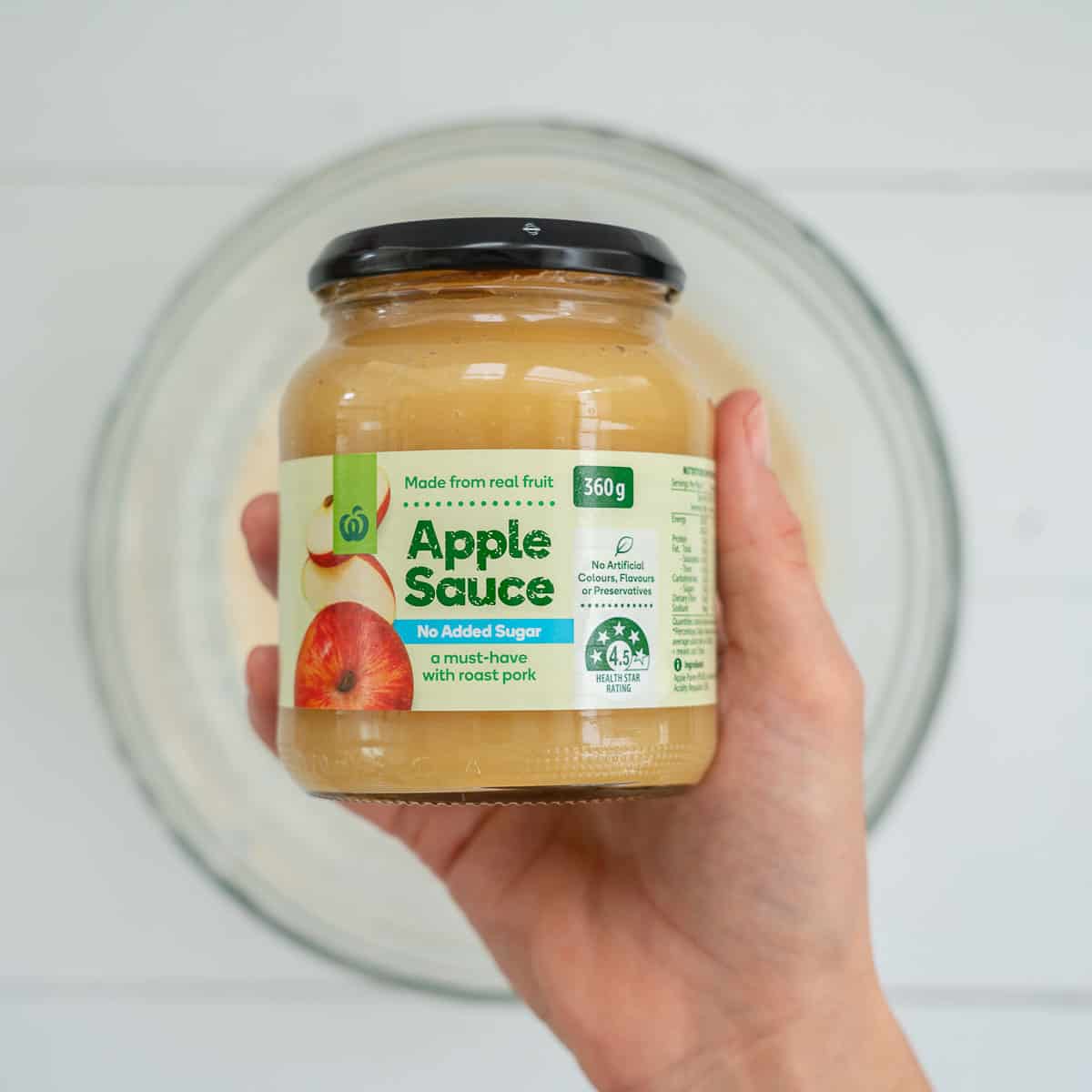 A jar of unsweetened apple sauce being held above a mixing bowl