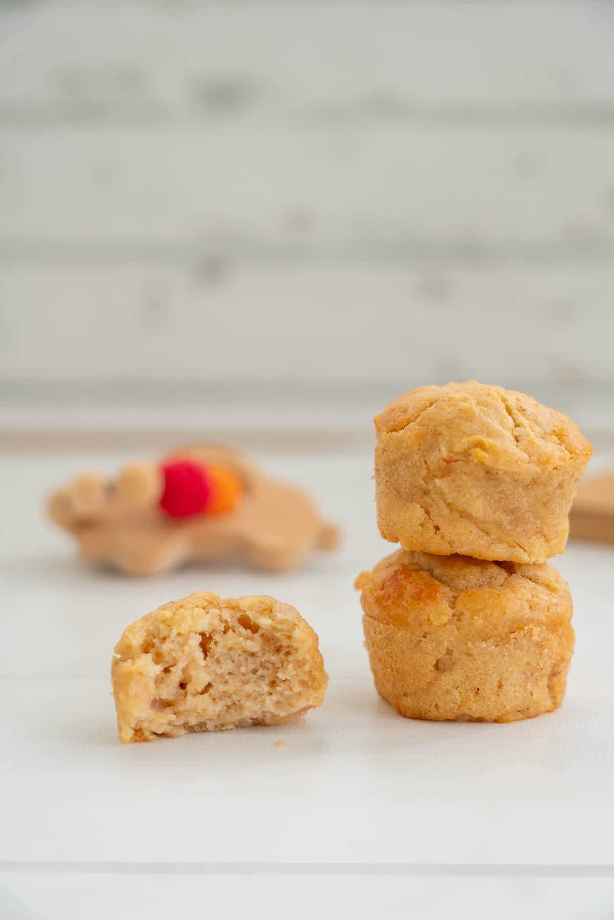 A stack of two mini muffins sitting next to half a muffin on a white bench top.