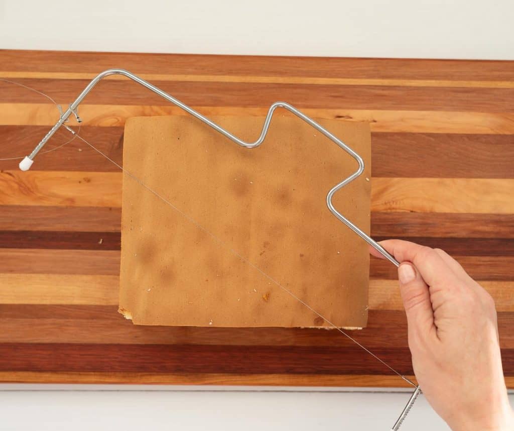 square sponge cake on a wooden chopping board with a cake leveler