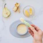 A spoonful of baby custard being held up above a bowl of custard.