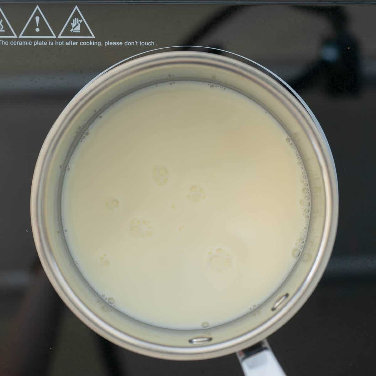 A saucepan of milk heating on a stove top.