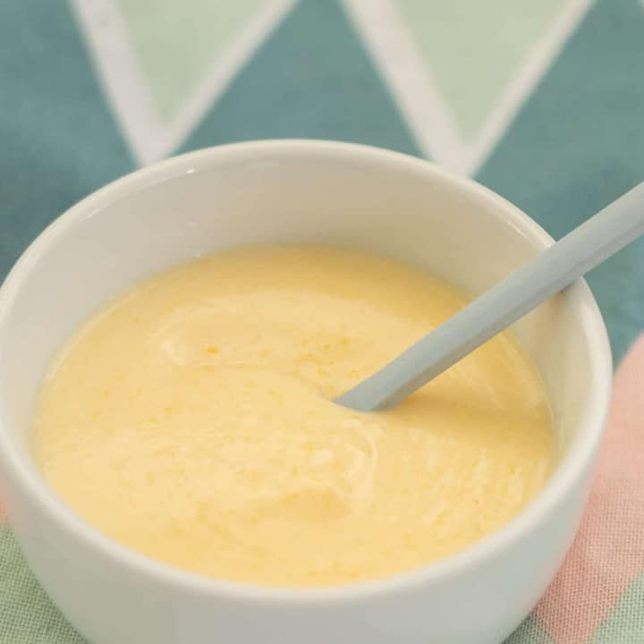 custard in a small white bowl with a blue spoon