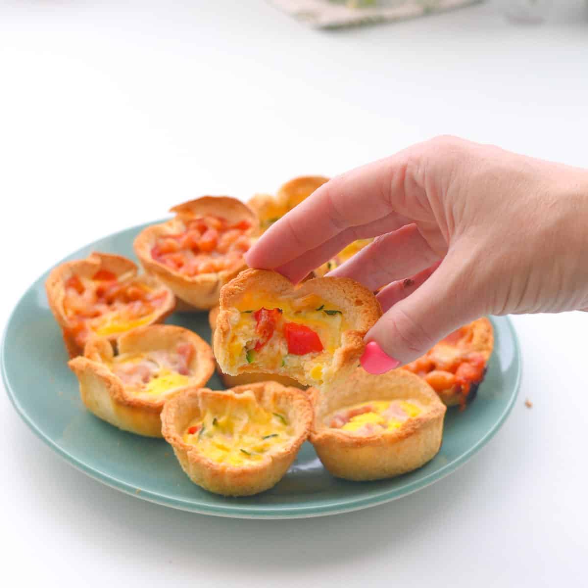 A turquoise plate filled with mini quiches with different fillings with one cut in half to show the inside.