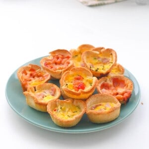 A turquoise plate filled with mini quiches with different fillings.