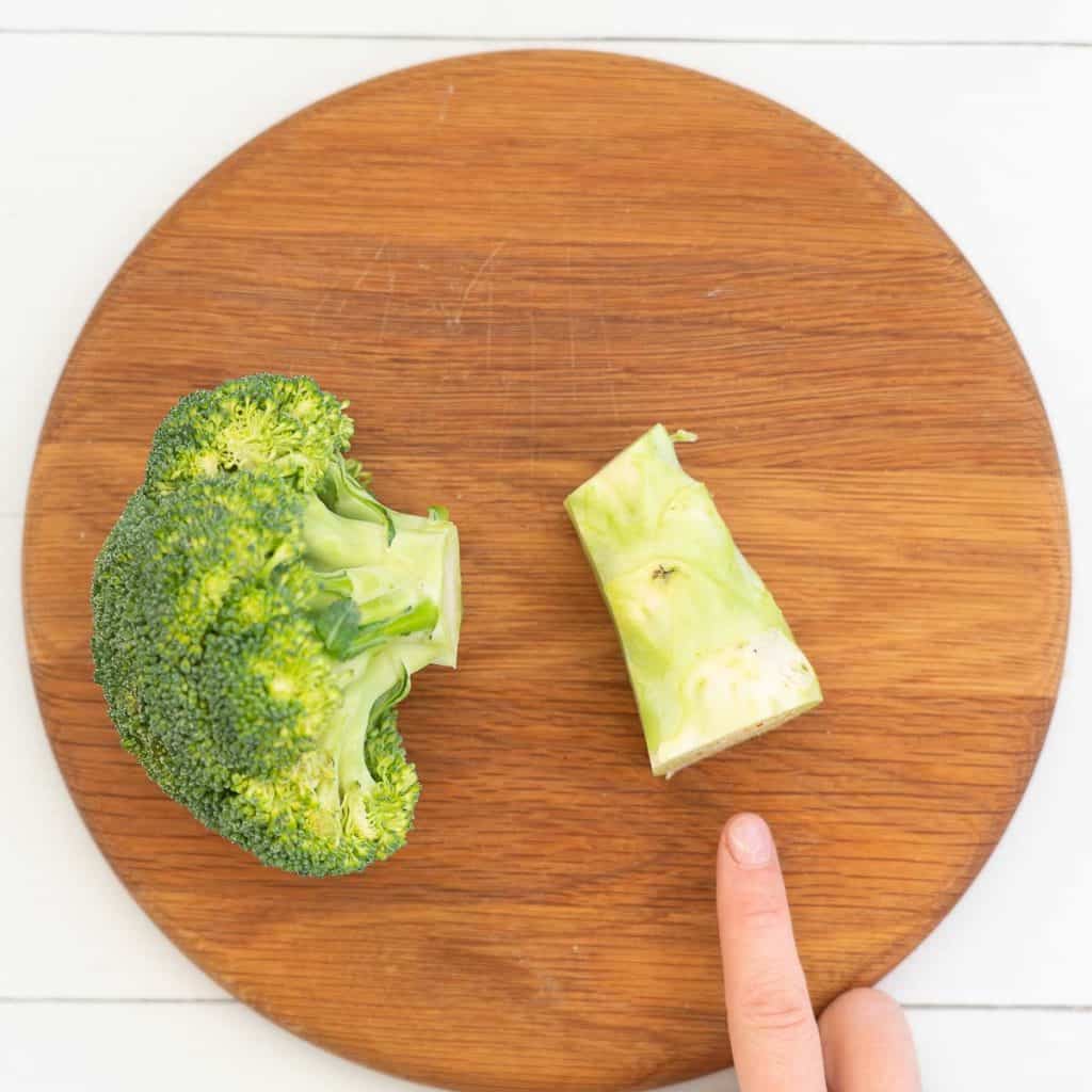 A head of broccoli on a chopping board with the stalk removed and sitting next to the florets