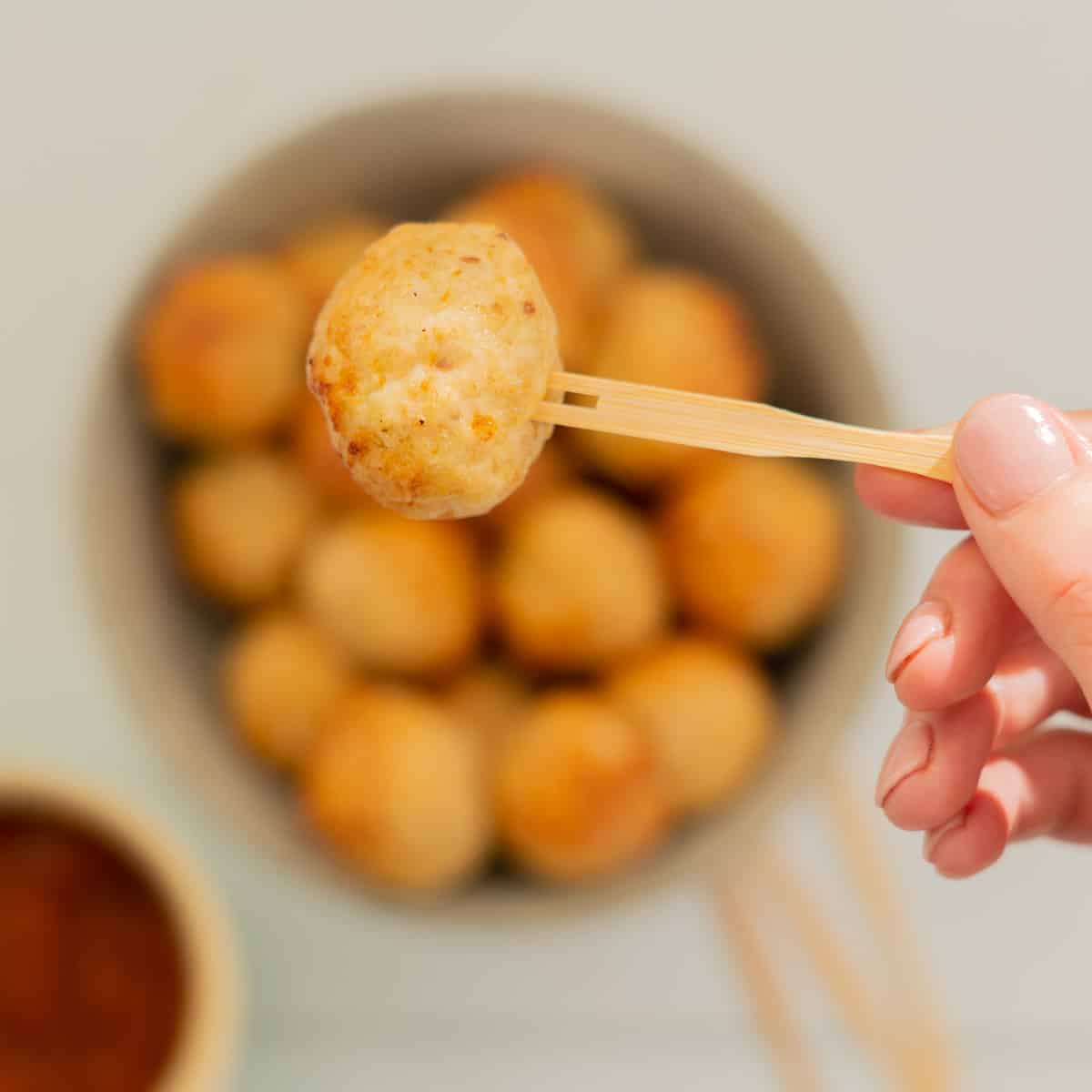 Chicken meatball on a bamboo fork being held above a bowl of meatballs