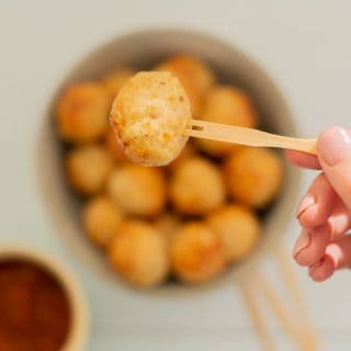 Chicken meatball on a bamboo fork being held above a bowl of meatballs