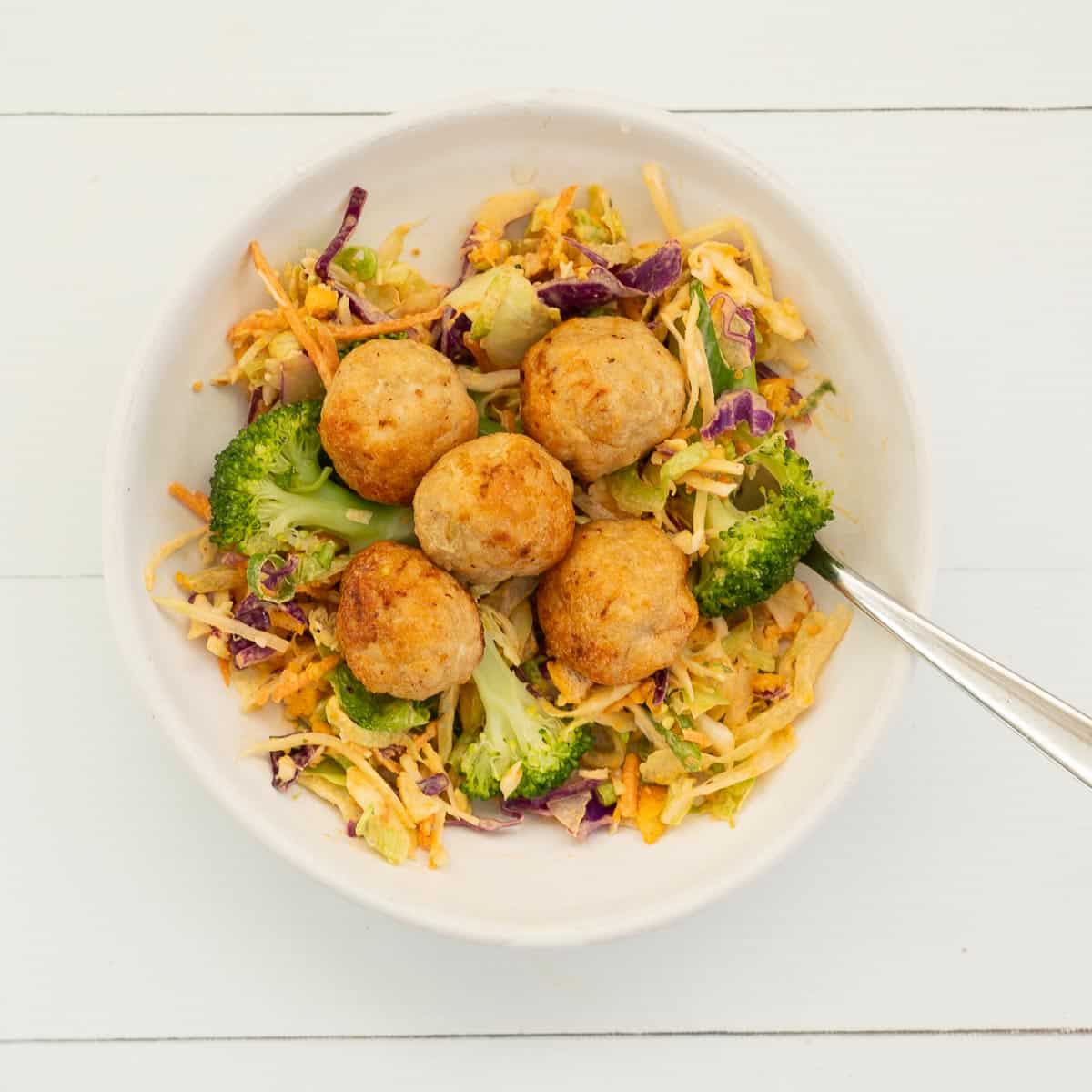 A white bowl filled with coleslaw, broccoli and 5 chicken rissoles