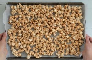 caramel covered popcorn spread out on a baking paper lined baking tray