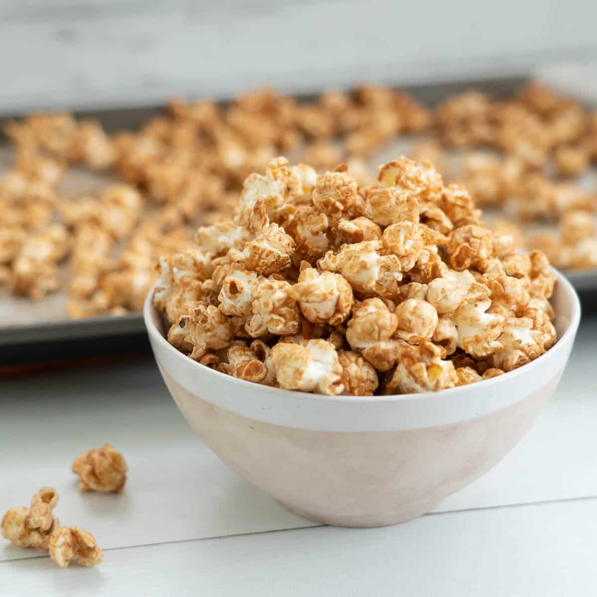 A bowl of cinnamon popcorn sitting in front of a baking tray of cinnamon popcorn.