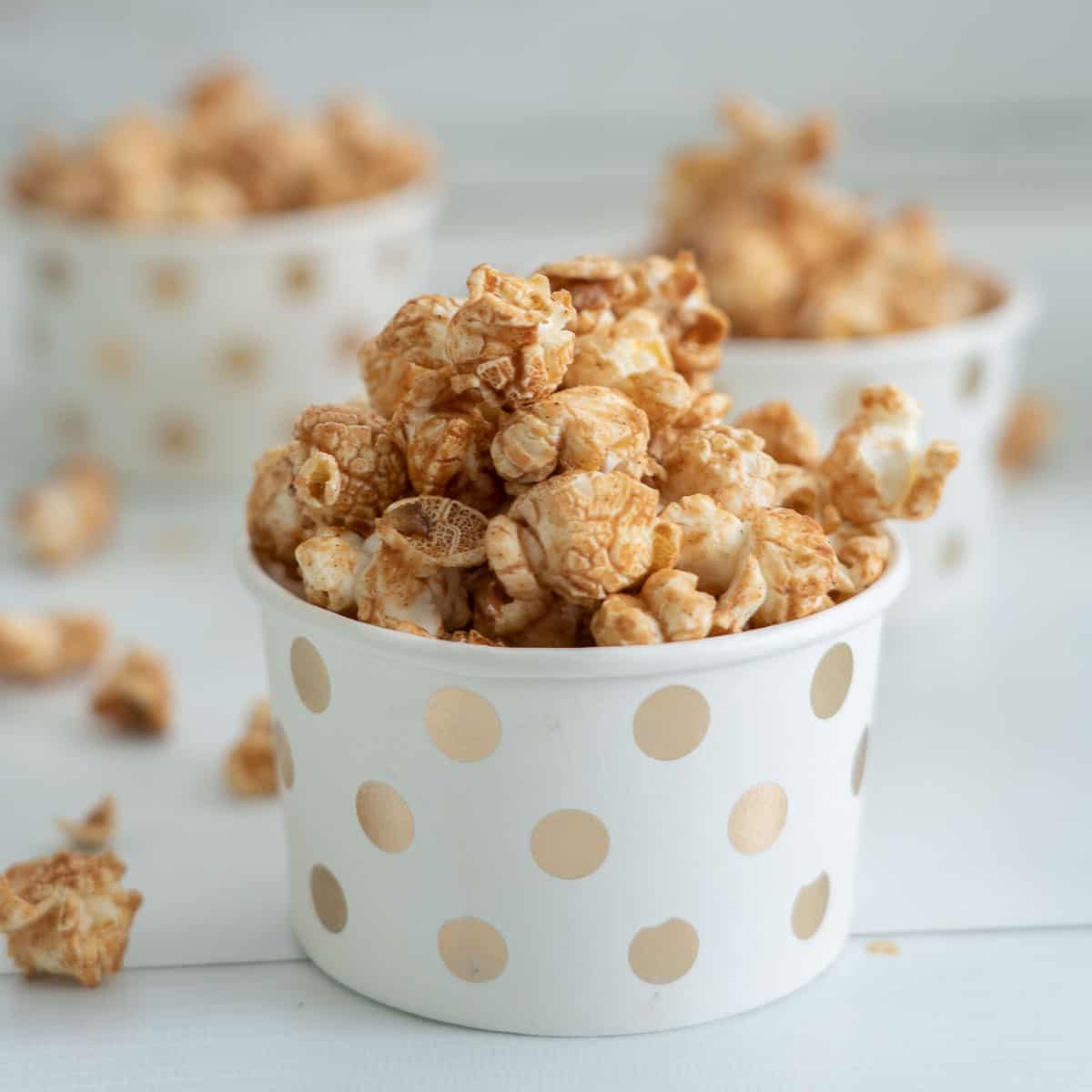 Cinnamon popcorn served in small white paper cups decorated with golden spots.