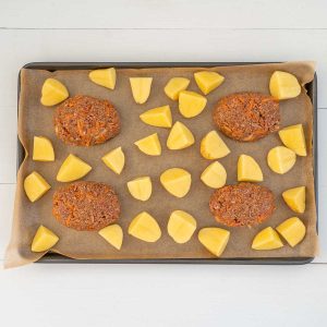 4 mini meatloaves and potatoes on a lined baking tray ready to go in the oven