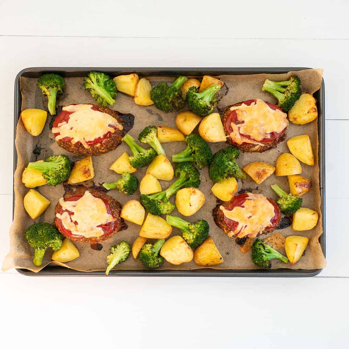 4 mini meatloaves toped with melted cheeseon an oven tray roast potatoes and broccoli 