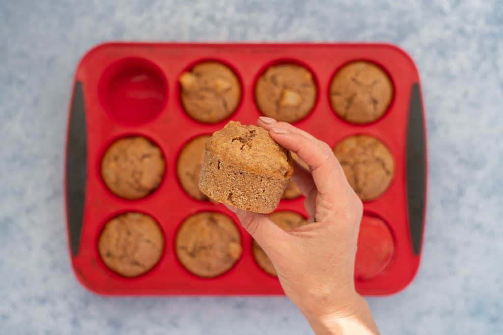 a cooked muffin after being popped out of the silicone muffin tray being held up above the tray of remaining muffins