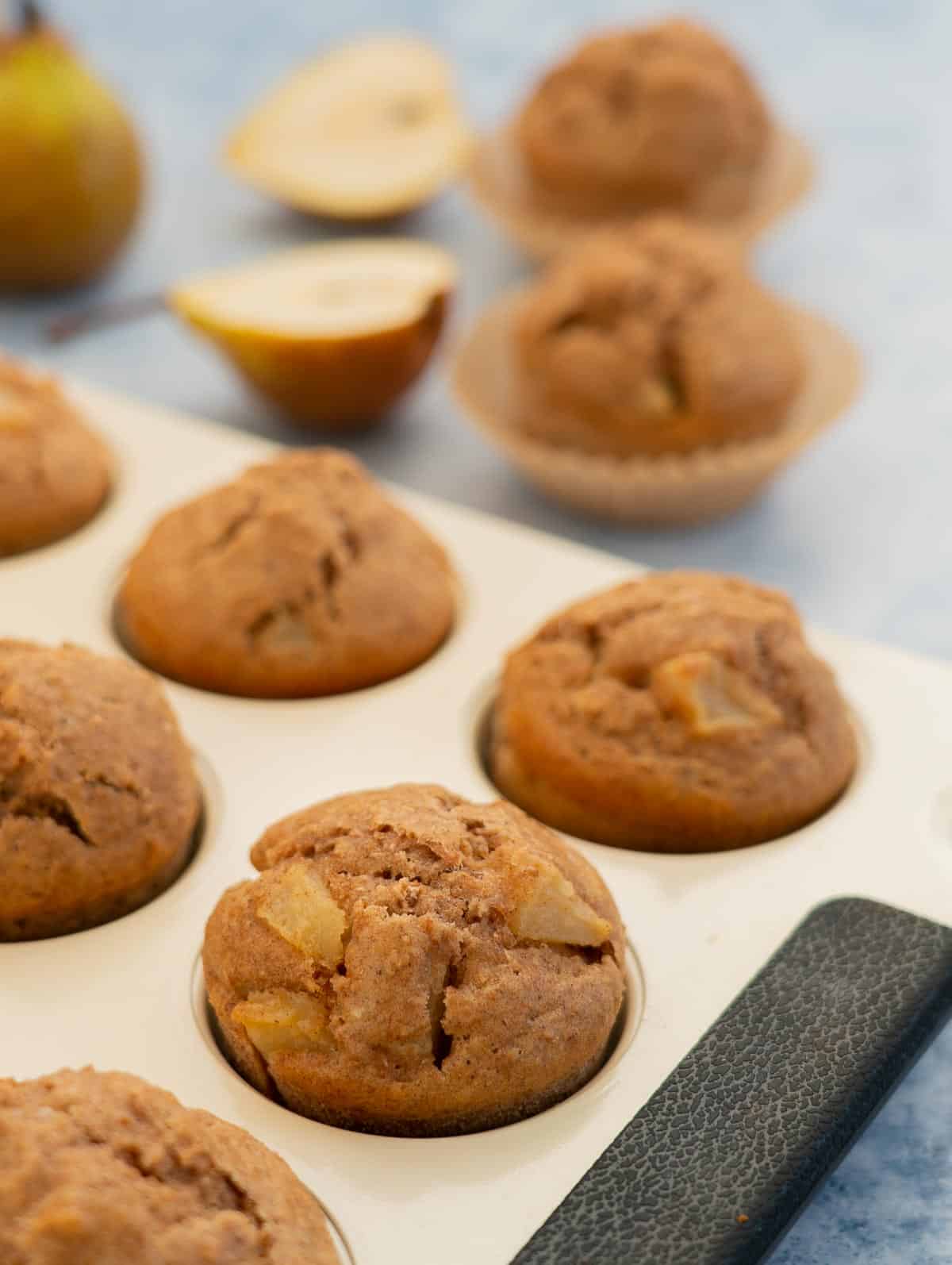muffins in a cream muffin tin, chunks of diced pear visible on the top of the muffins