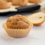 pear muffin in a muffin case on a marble bench top with a sliced pear in the background