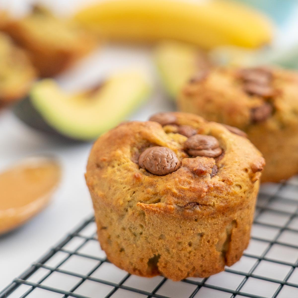 muffin sitting on a cooling rack, avocado and banana visible in the background