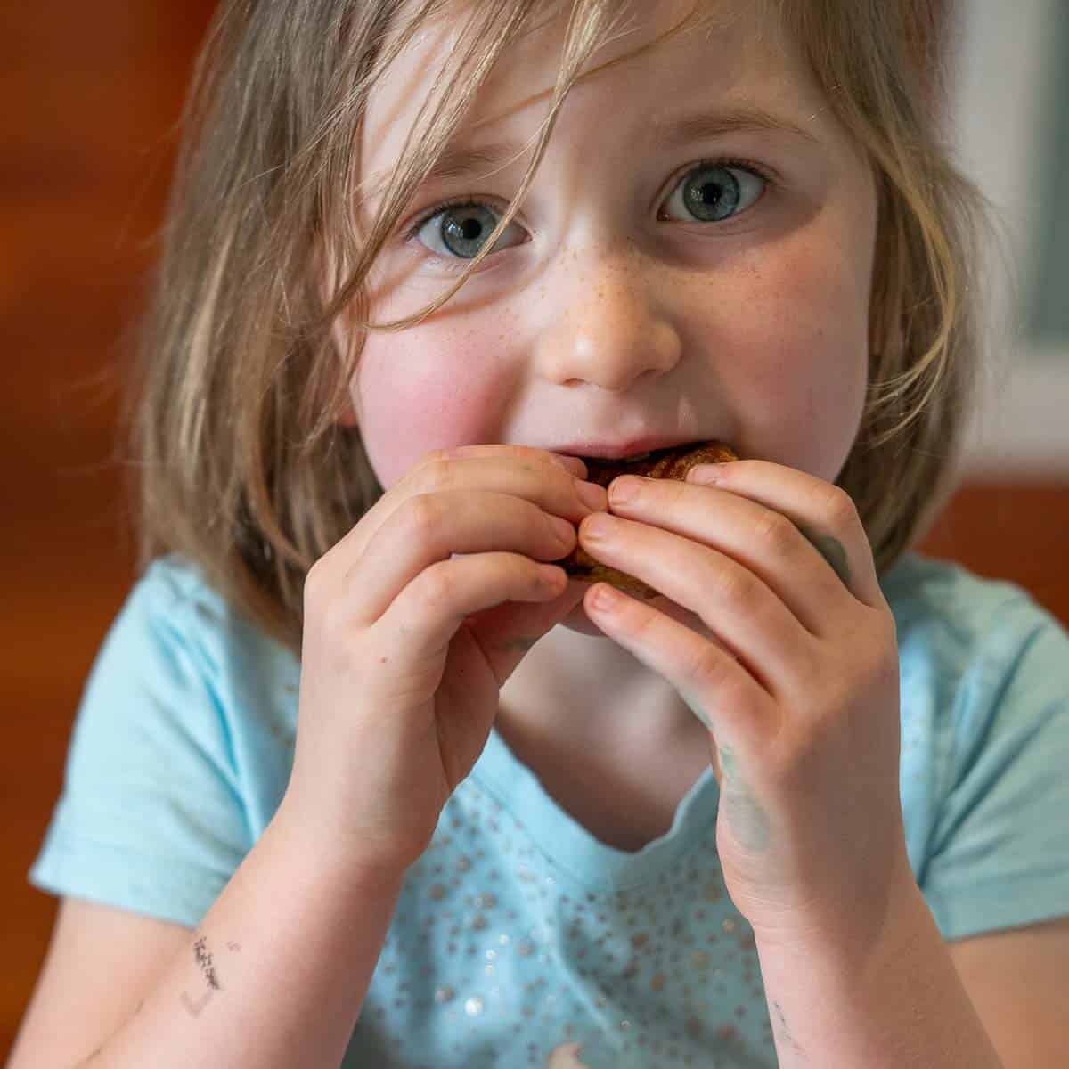 a young girl in a blue t-sirt biting into a cookie