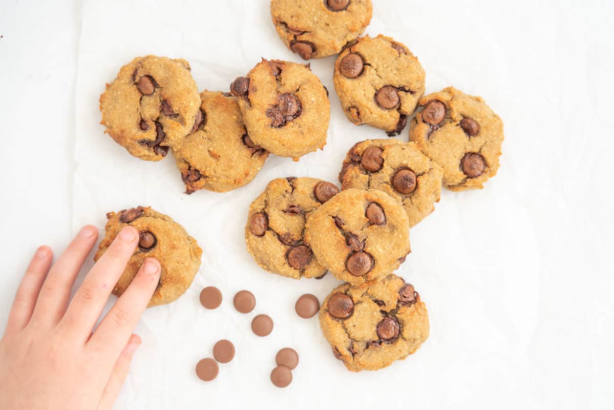 A child's hand reaching out for chocolate chip chickpea cookies lying on baking paper