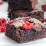 close up of a piece of chocolate brownie on a white bench top with milk and raspberries