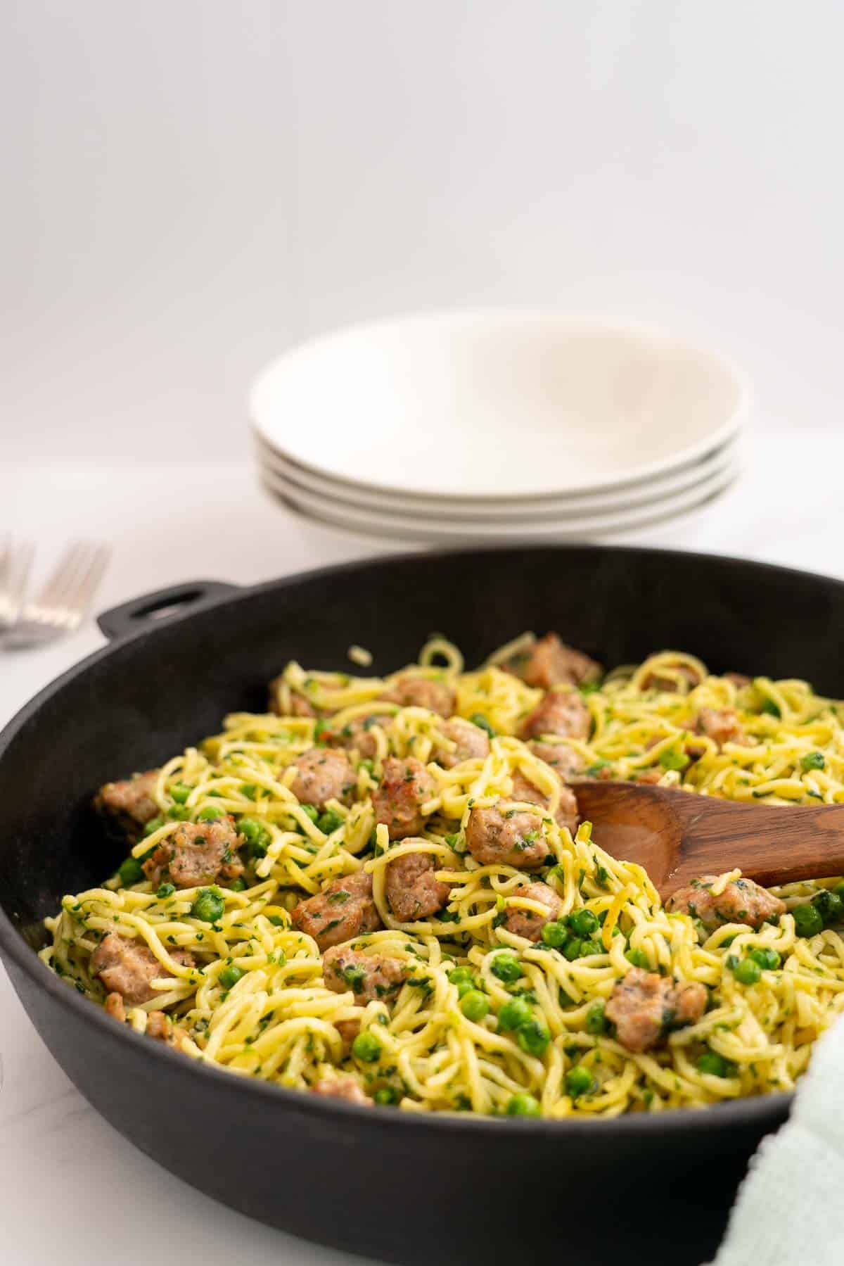 Golden Fried Spaghetti in a large skillet with sausage peas and spinach, serving bowls and cutlery in the background