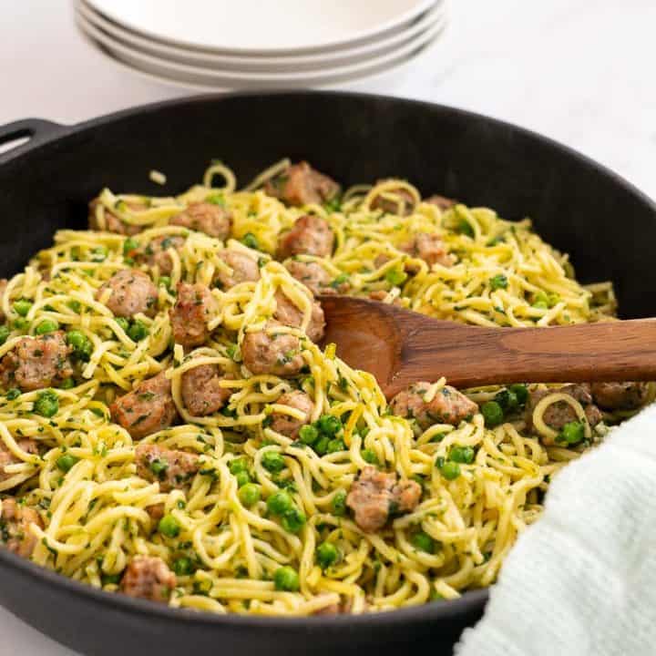 Golden Fried Spaghetti in a large skillet with sausage peas and spinach, serving bowls and cutlery in the background