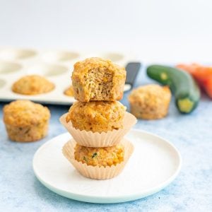 3 savoury muffins staked on top of each other, muffin tray and vegetables in the background