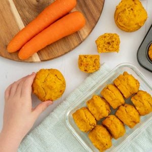 8 carrot muffins in a container with a child's hand reaching for a muffin