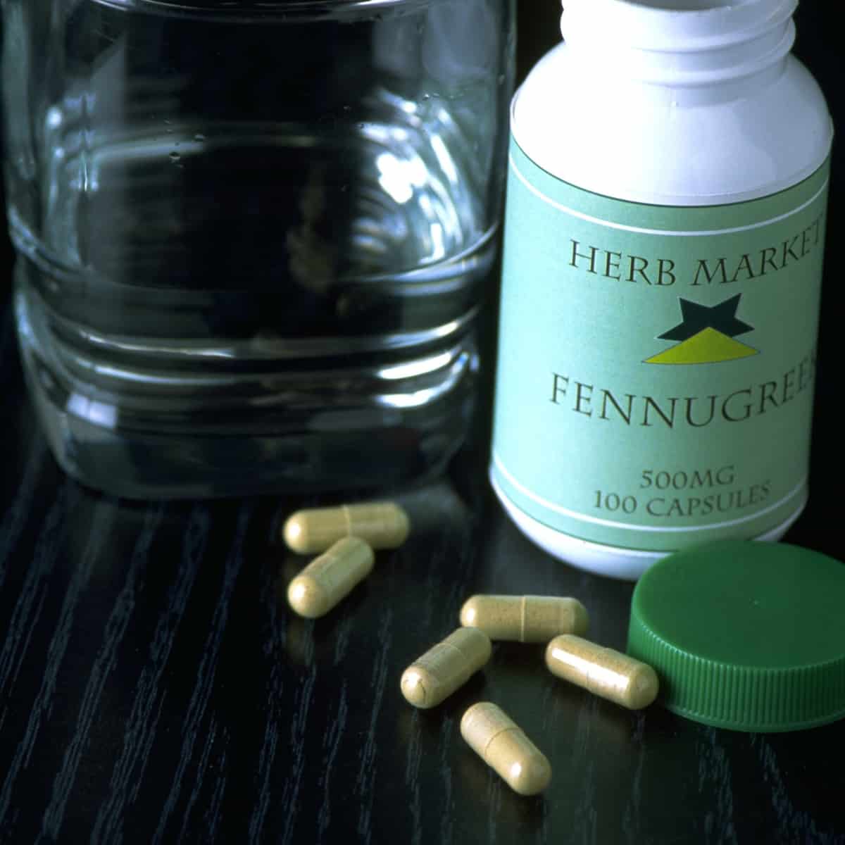 medication bottle of fenugreek capsules sitting next to a glass of water
