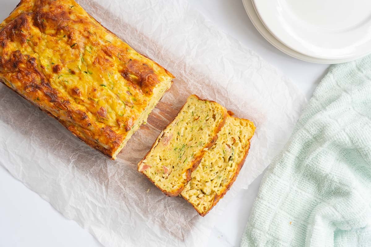 Top down shot of baked zucchini slice on a chopping board, 2 slices removed from the end of the loaf