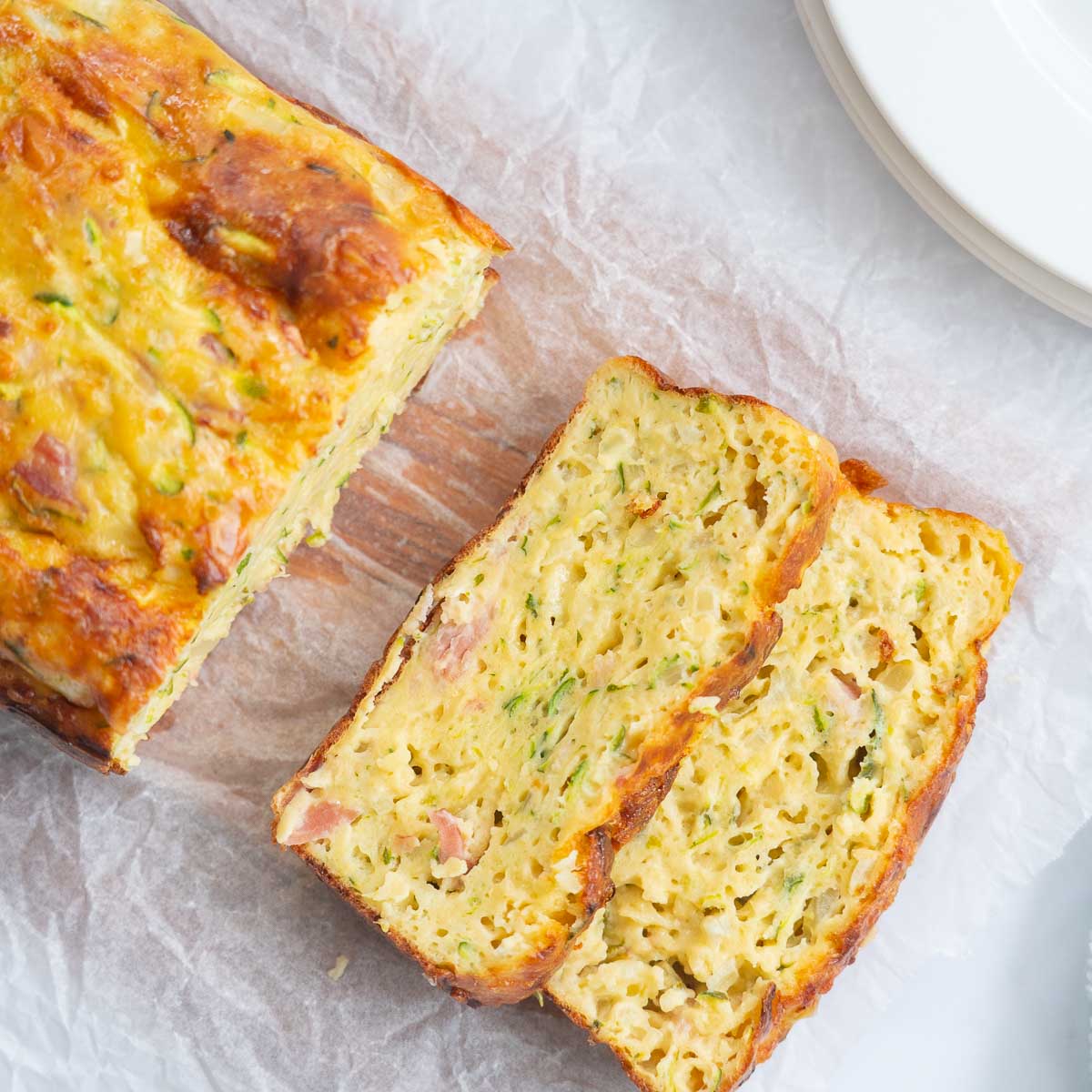 Top down shot of baked zucchini slice on a chopping board, 2 slices removed from the end of the loaf