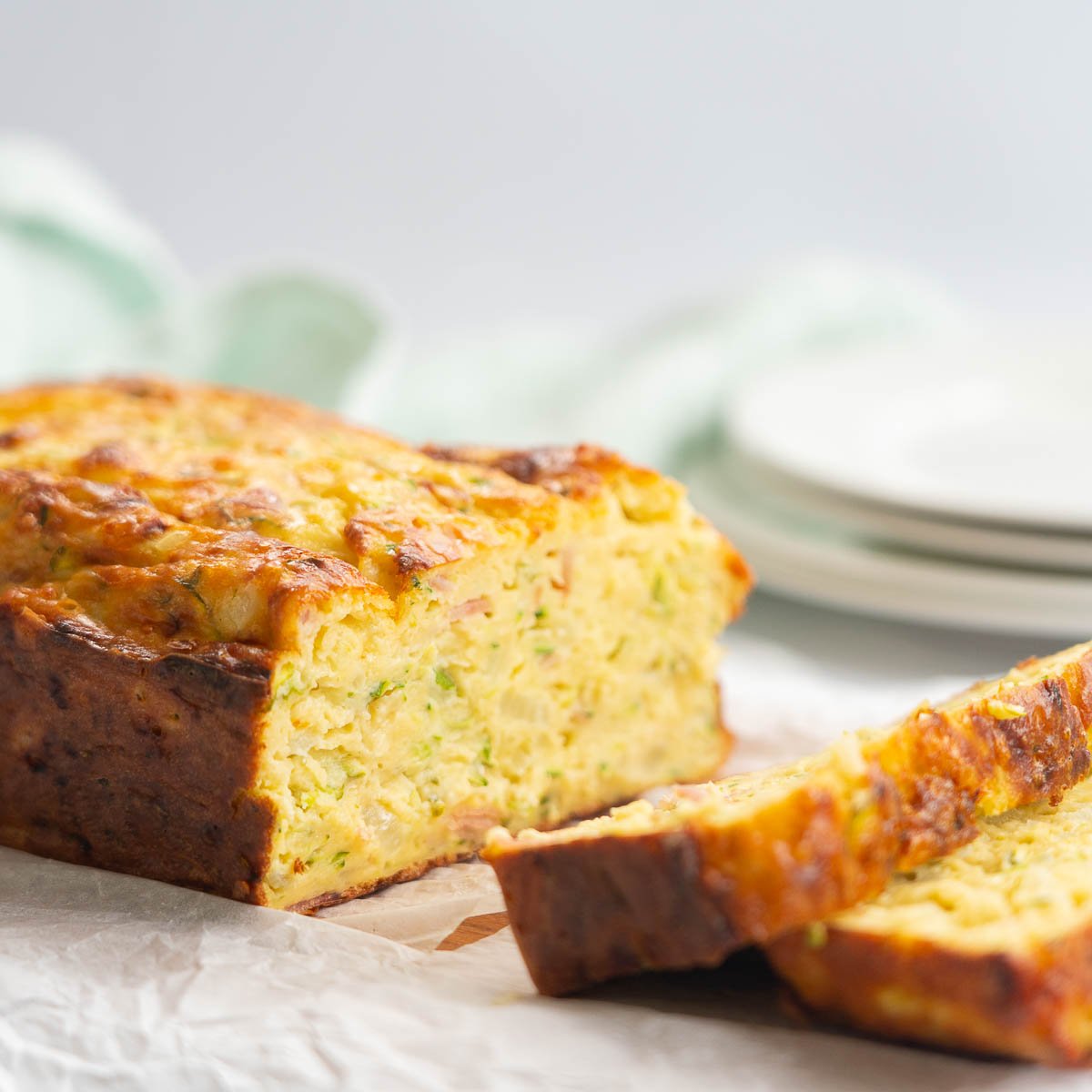 zucchini slice on a chopping board sliced so that you can see the inside, plates and a tea towel in the bacground