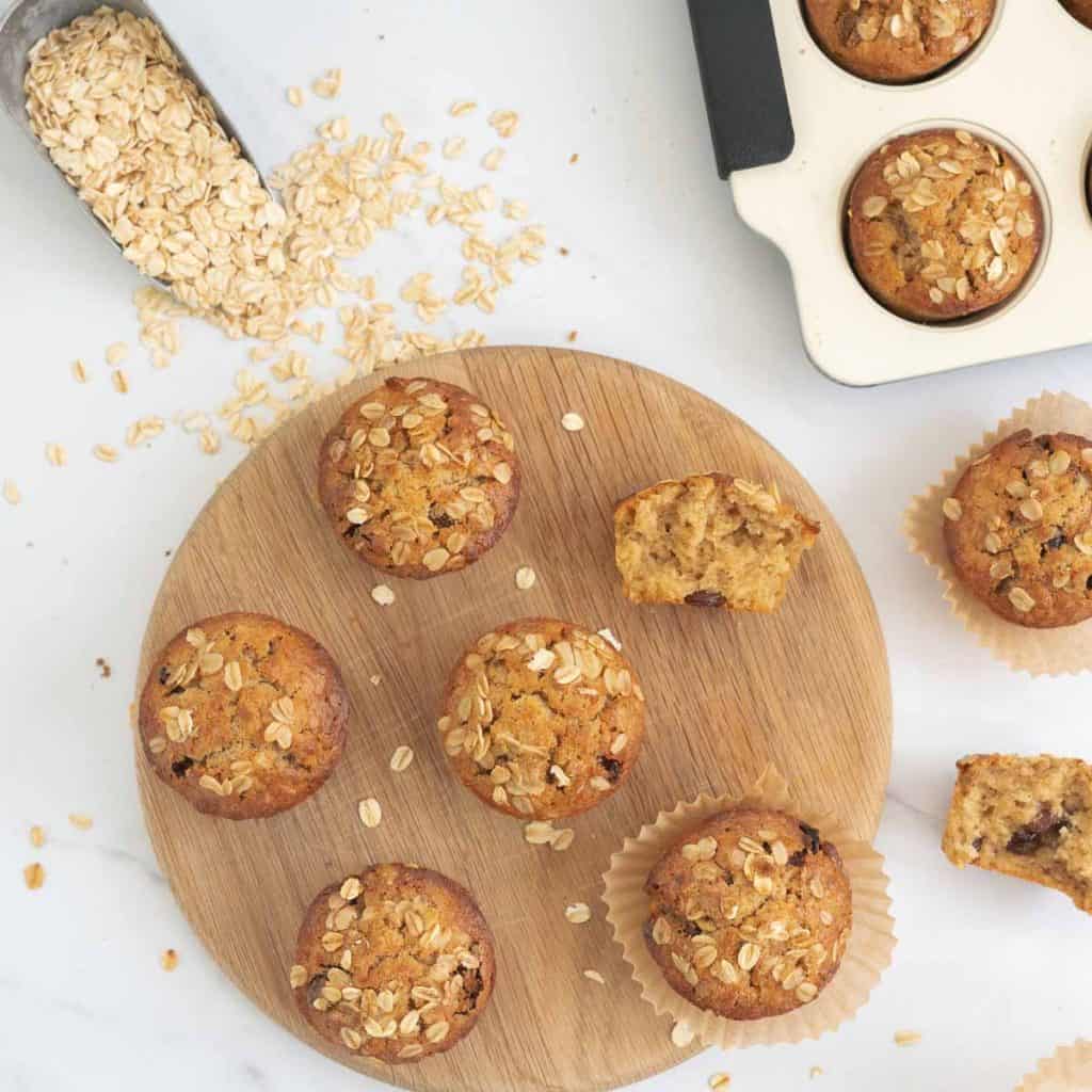 top down shot of oatmeal muffins on a round wooden tray with a scoop of rolled oats