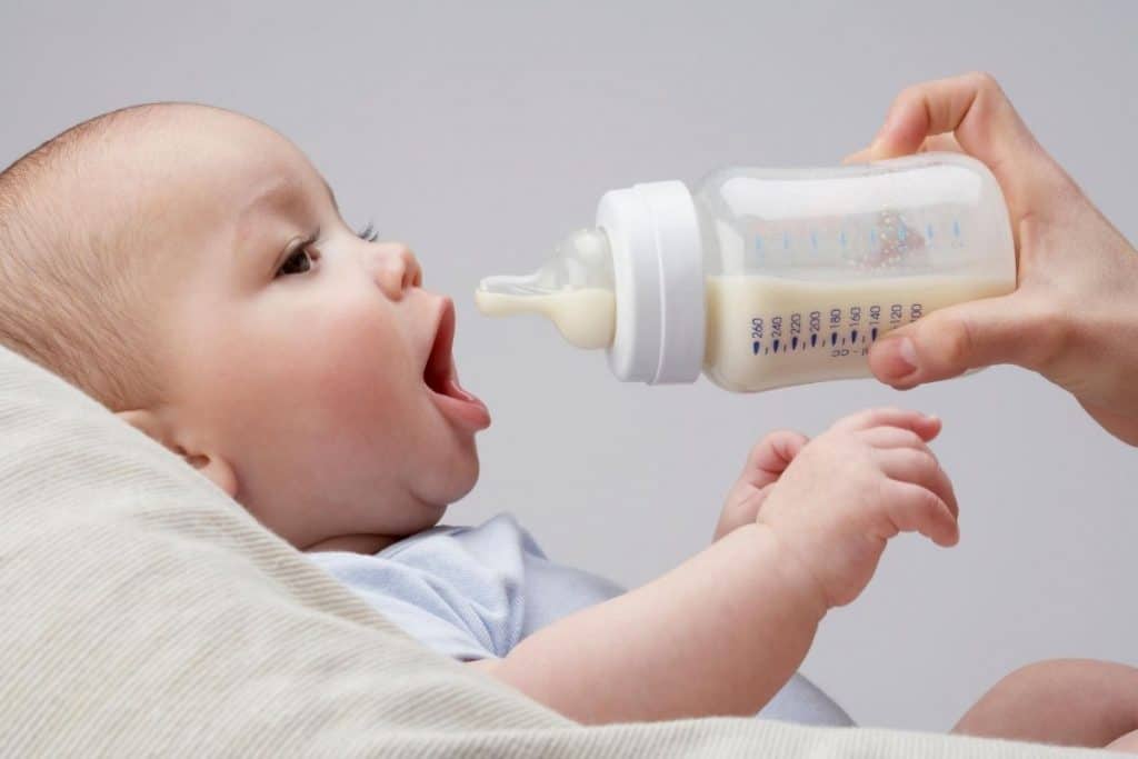 baby with mouth open being offered a baby bottle
