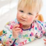 toddler in a colourful bib eating a fruit gummy